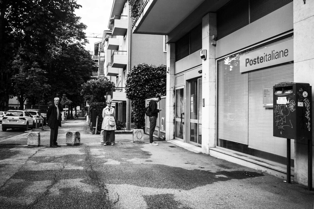 Tre persone attendono in coda l'apertura dell'Ufficio postale. Street Photography, Black and White.