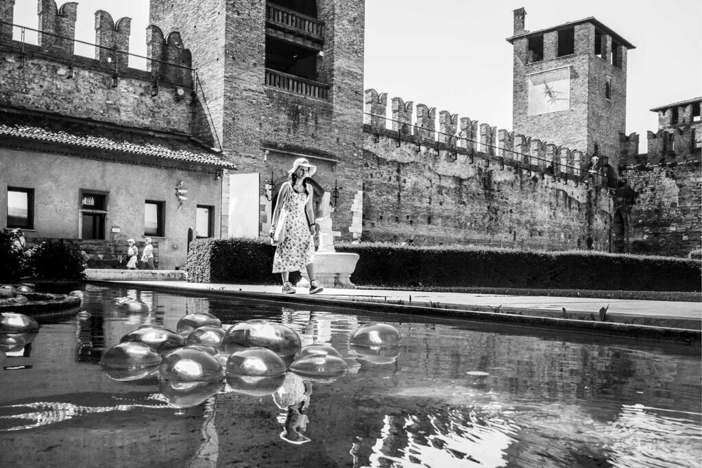 Una turista a Castelvecchio (Verona) si specchia nell'acqua. Street Photography, Black and White.