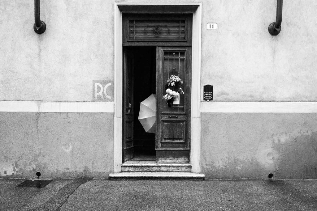 L'ombrello si apre dietro il portone per affrontare una giornata di pioggia. Street Photography, Black and White.