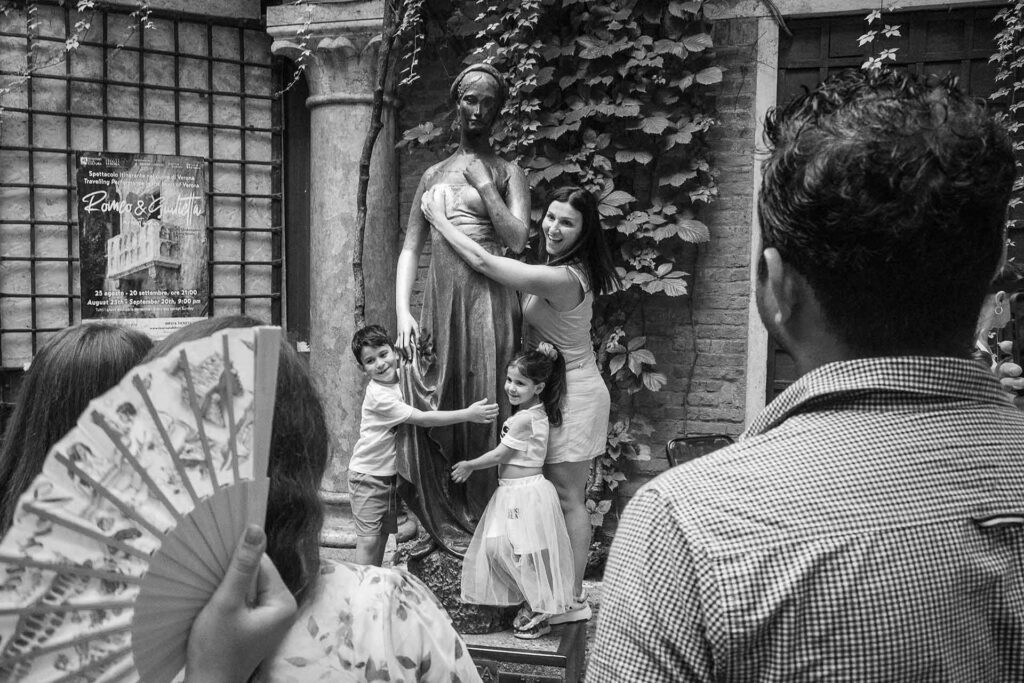 Mamma e figli abbracciano la statua di Giulietta a Verona. Street Photography, Black and White.