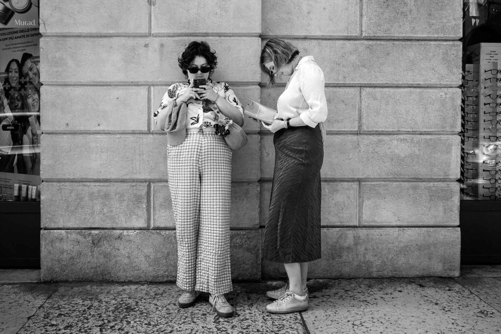 Due ragazze incorniciate da un muro in pietra. Street Photography, Black and White.