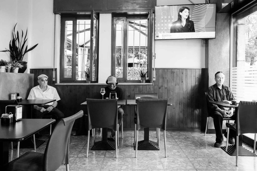 Presenze all'interno di un bar voltano le spalle alla TV. Street Photography, Black and White.