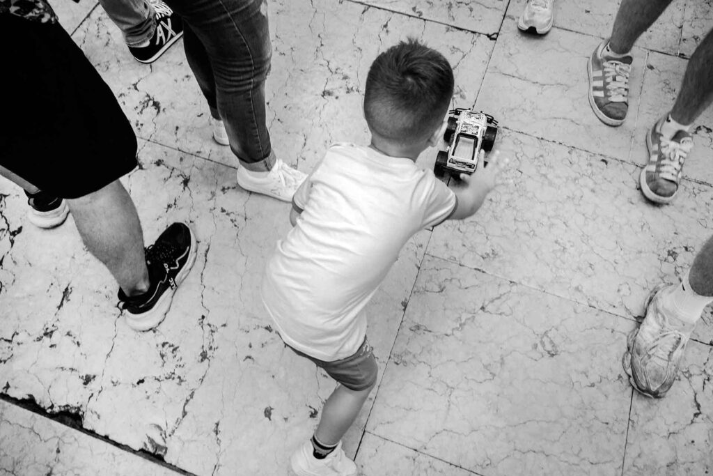 Bambino gioca con la sua macchinina dribblando tra i piedi dei tanti pedoni. Street Photography, Black and White.