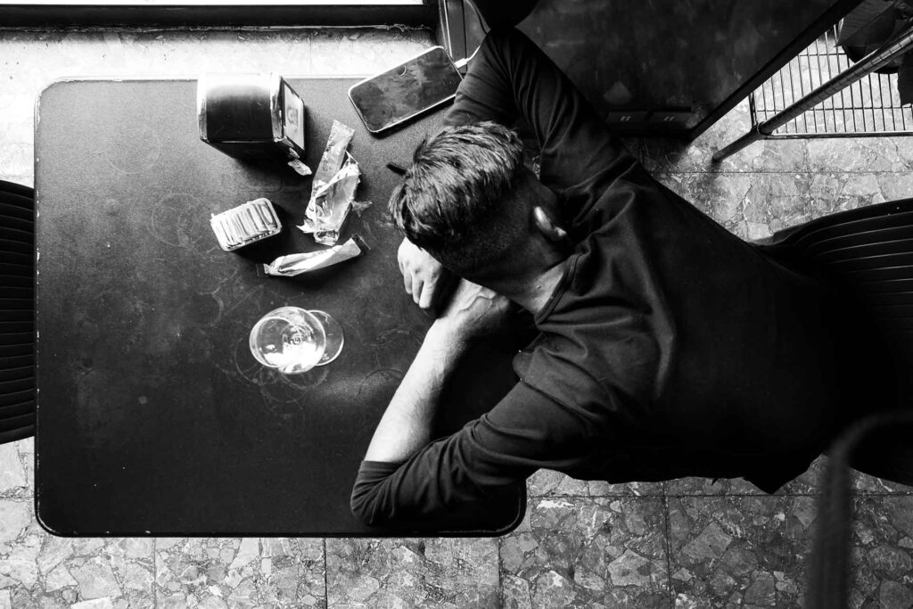 Ragazzo al bar mentre dorme con il capo chino sul tavolino. Street Photography, Black and White.