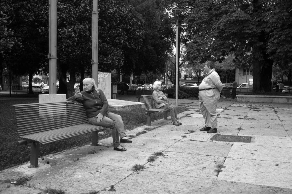 Presenze all'interno di un giardino, tre individui vicini ma non dialoganti. Street Photography, Black and White.