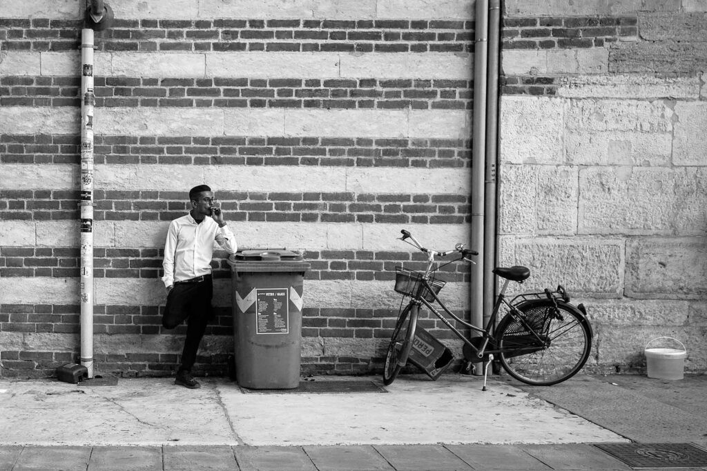 Un ragazzo, dietro l'angolo, si concede una pausa temporanea dal lavoro. Street Photography, Black and White.