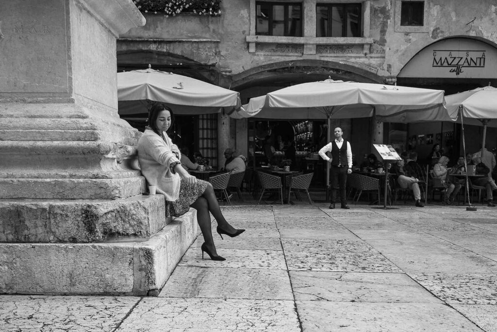 Una donna seduta sotto a un monumento e un uomo, un barista, in piazza. Street Photography, Black and White.