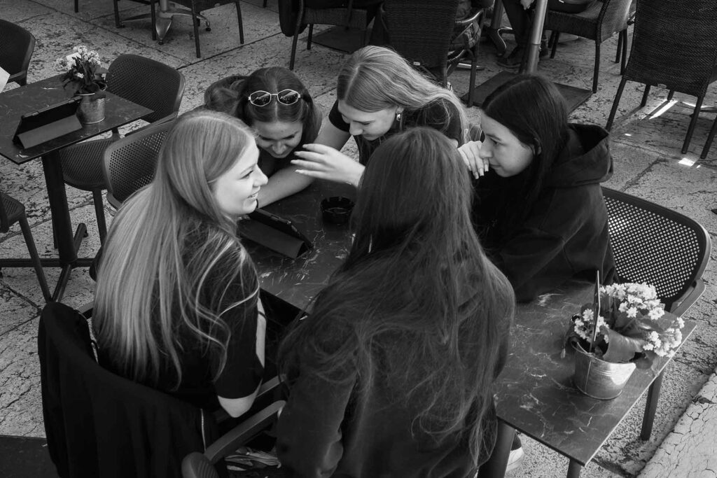 Quattro amiche sedute al tavolino di un bar sembrano confidarsi segreti. Street Photography, Black and White.