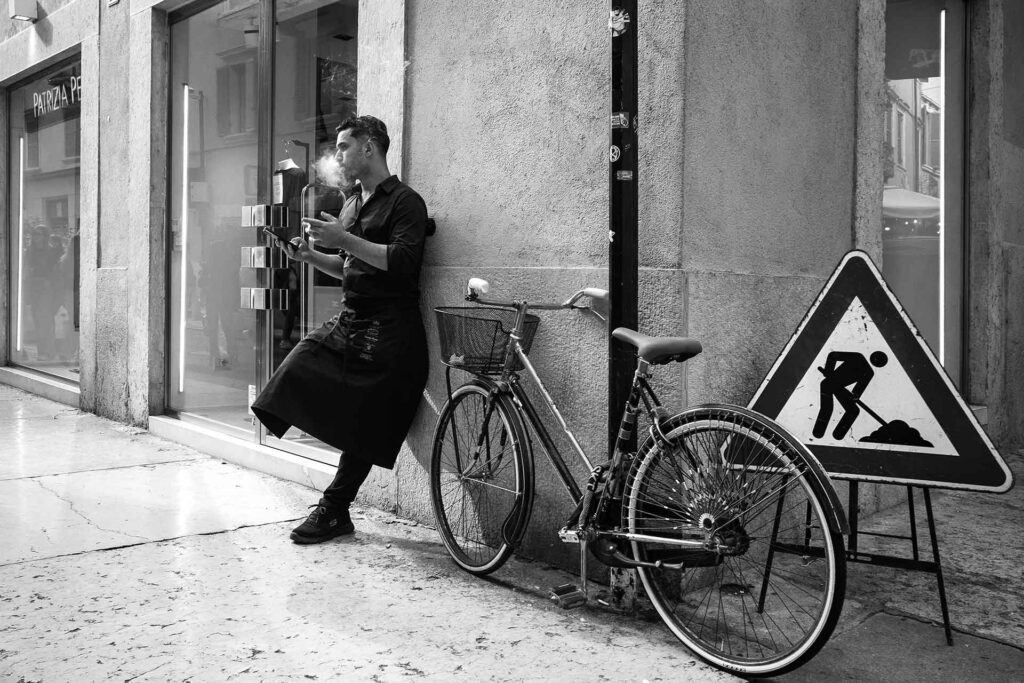 Un lavoratore fuori dal negozio si concede una pausa in una nuvola di fumo. Street Photography, Black and White.