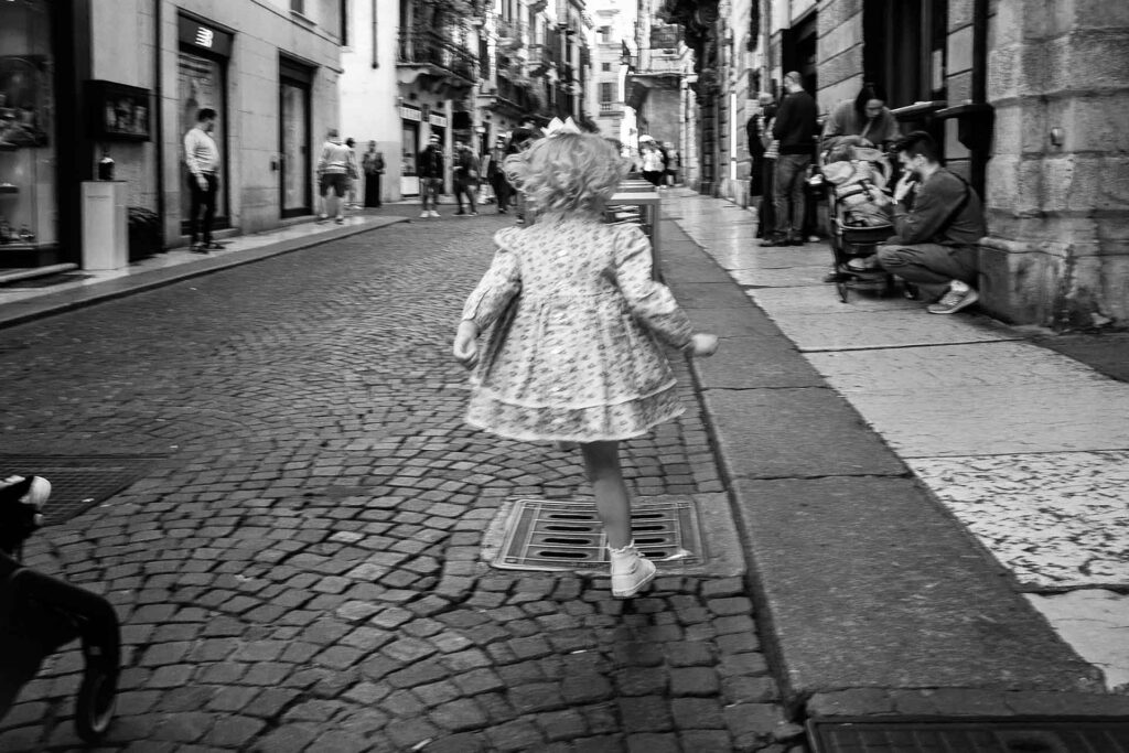 Una bambina saltella sulle gambe. Street Photography, Black and White.