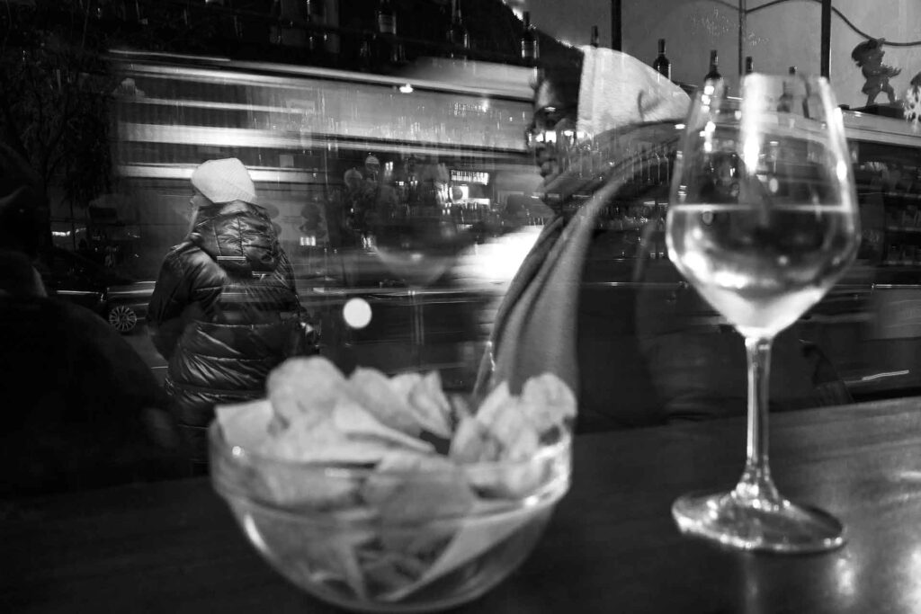Interno ed esterno del bar, la vetrina come filtro trasparente tra quiete e movimento. Street Photography, Black and White.