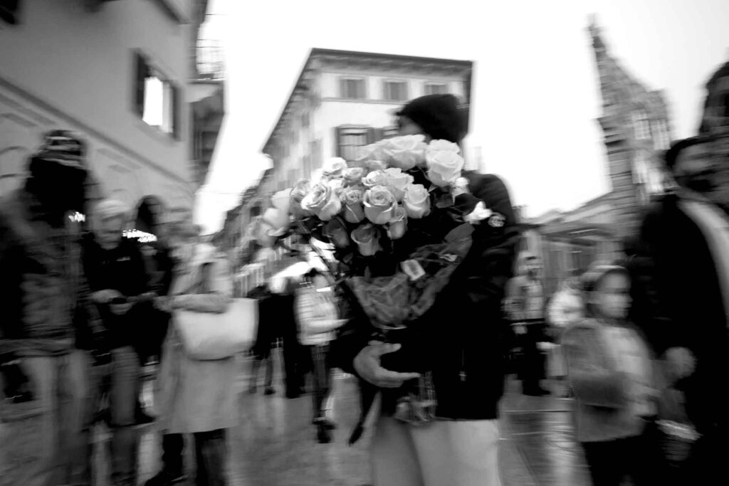 Venditore di rose in un via vai di turisti distratti (sfocati). Street Photography, Black and White.