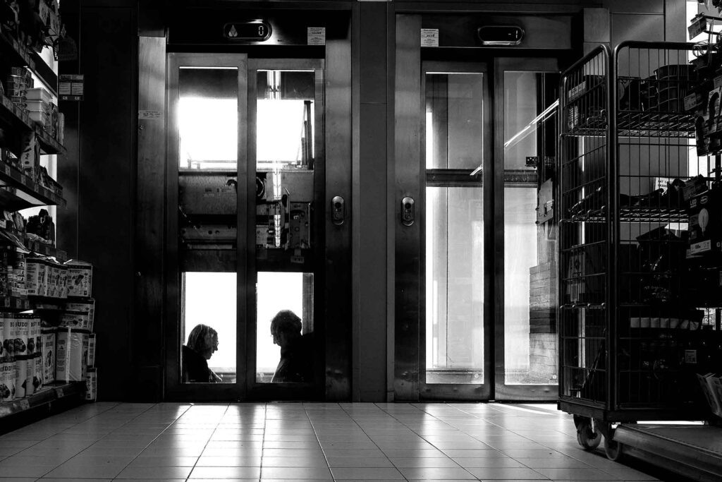 In un supermercato due signori scendono (o salgono?) con l'ascensore. Street Photography, Black and White.