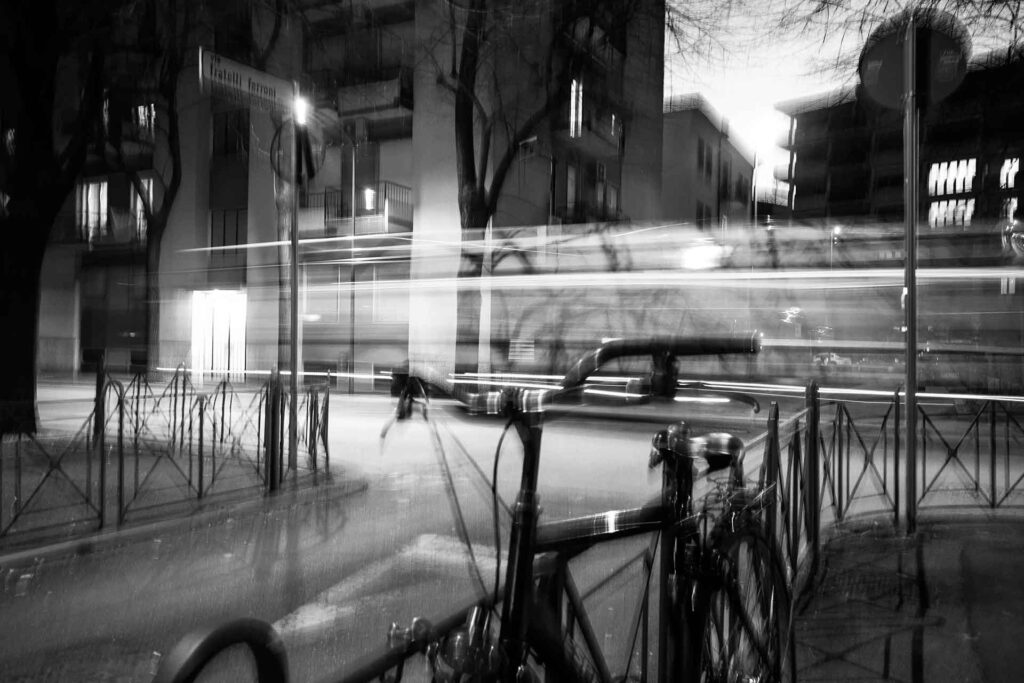 Incrocio di notte, scia luminosa di un autobus di passaggio, bicicletta