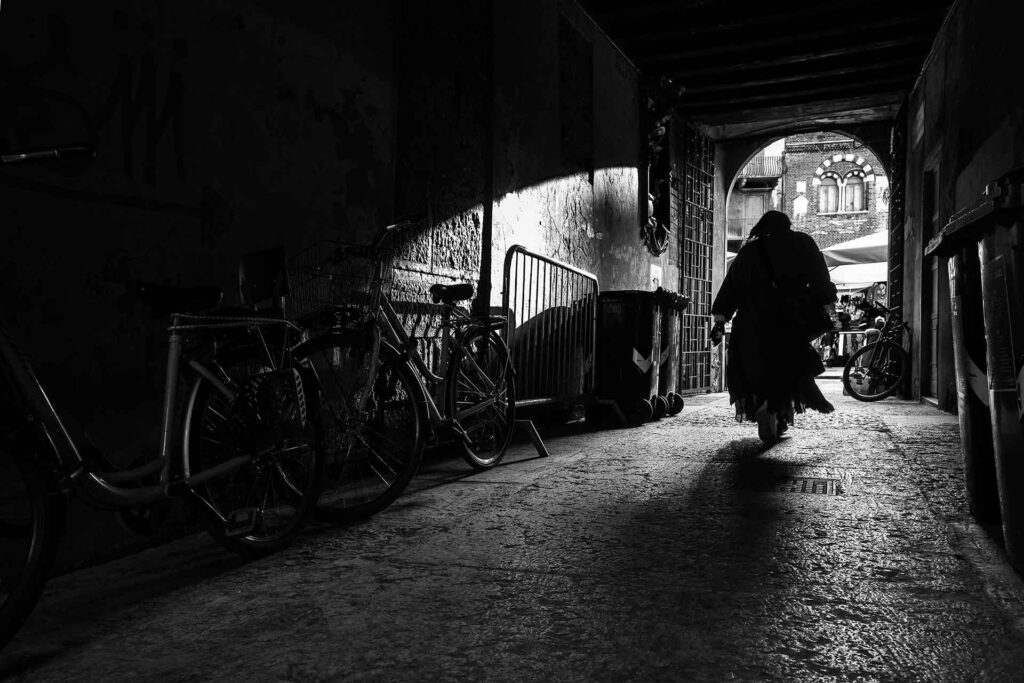Una donna percorre un sottoportico tra suggestivi contrasti di luci e ombre. Street Photography, Black and White.